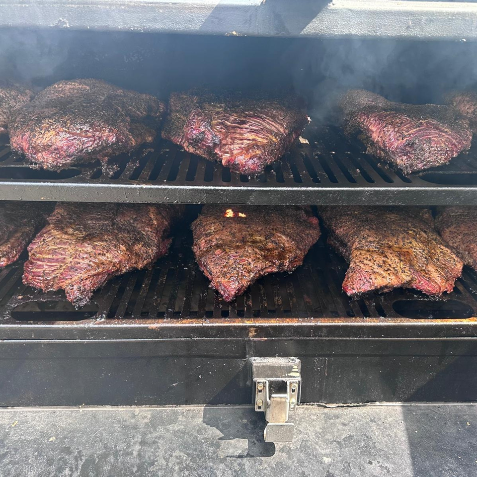 Multiple large cuts of seasoned brisket smoking on a two-tier grill inside a dark smoker.