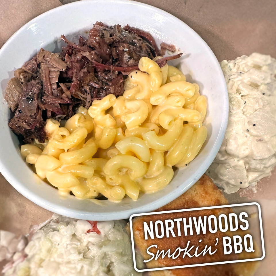 A white bowl of Northwoods Smokin' BBQ pulled pork and macaroni and cheese, with sides.