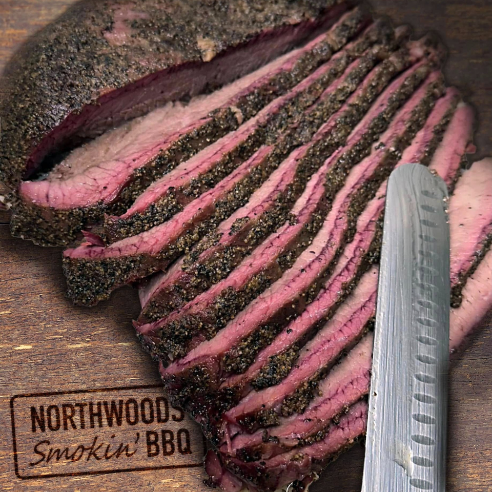 Slices of Northwoods Smokin' BBQ brisket with a dark, peppery crust and pink interior, on a wooden board.